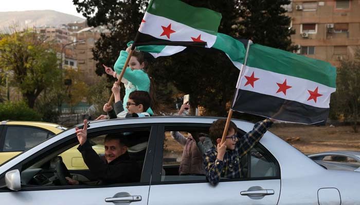 People celebrate with the Syrian opposition flag, in Damascus, on December 10, 2024. — AFP