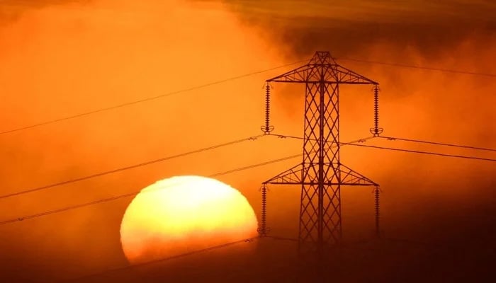 The sun sets behind an electricity pylon, as fog develops, near Petersfield, Britain, December 1, 2022. — Reuters