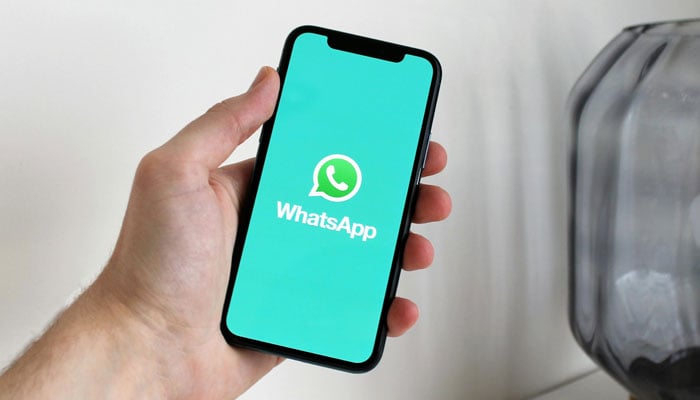 A representational image shows a person holding a phone with the WhatsApp logo displayed on it. — Pexels