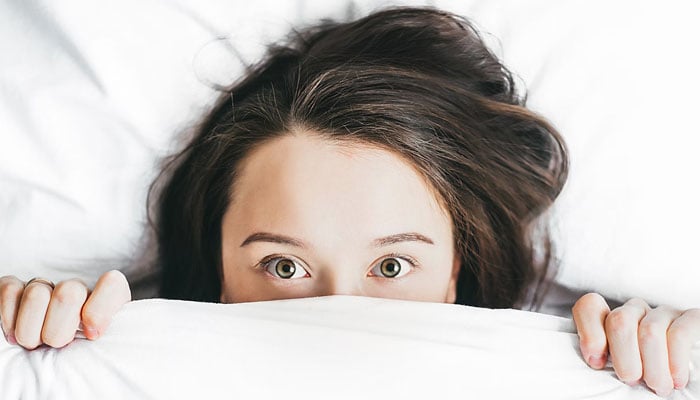 A representational image showing a person lying on her bed under a blanket. — Unsplash/File