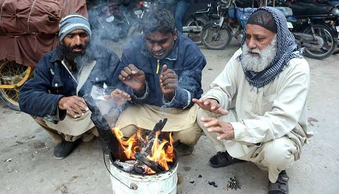 People sitting around wooden fire to keep them warm during prevailing cold weather. — APP/File