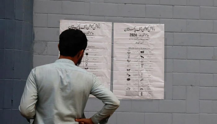 A man looks at the poster with the names of contesting candidates and their electoral signs, outside a polling office, set up for general election in Karachi, February 7, 2024. — Reuters