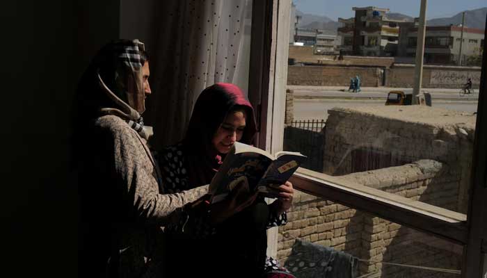 Hawa, 20, a third-year Russian literature student at the Burhanuddin Rabbani University (which was renamed by the Taliban to Kabul Education University), reads a book with her sister on a windowsill at their home in Kabul, Afghanistan, October 23, 2021. — Reuters