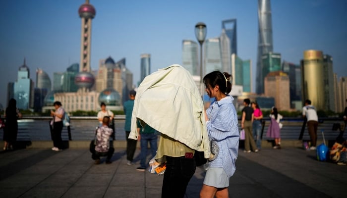 A person uses clothing to protect themselves from the sun, as they walk on the Bund on a hot day, in Shanghai, China May 15, 2023. — Reuters