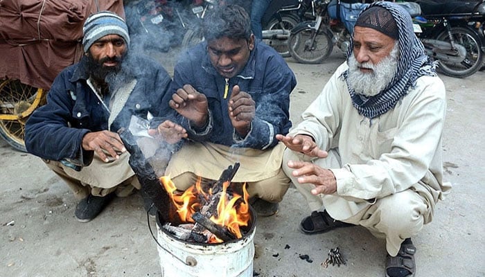 People sitting around a fire to keep them warm during chilly weather in Karachi. — APP/File