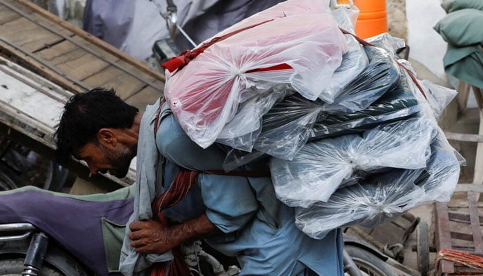 A labourer bends over as he carries packs of textile fabric on his back to deliver to a nearby shop in a market in Karachi. — Reuters/File