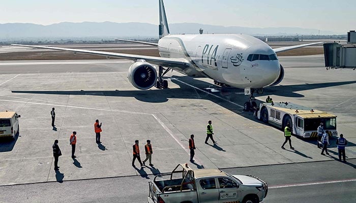 Ground staff stand next to the Pakistan International Airline aircraft ahead of its takeoff for Paris at the Islamabad International Airport on January 10, 2025. — AFP