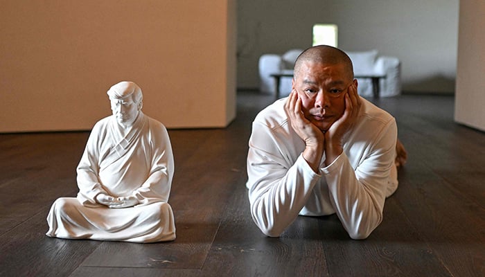 This photo taken on December 9, 2024 shows artist Hong Jinshi posing for photos next to a sculpture of US president-elect Donald Trump in a pose evoking the Buddha at his workshop in Xiamen, in southeastern Chinas Fujian province. — AFP