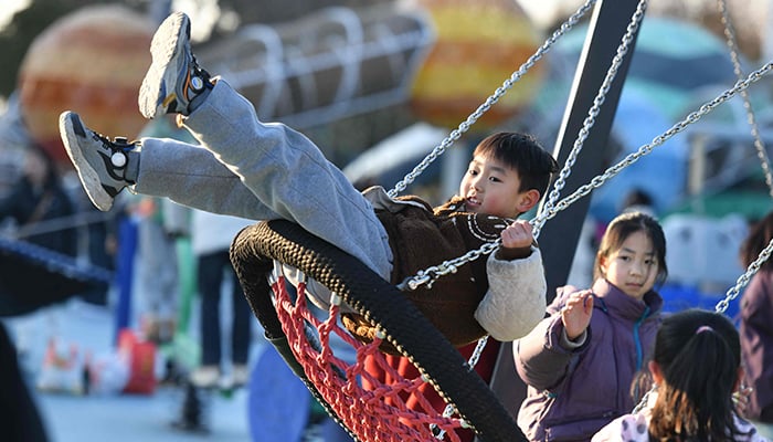 This photo taken on January 16, 2025 shows a boy (C) playing on a swing in a park in Fuyang, east Chinas Anhui province. — AFP