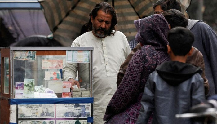 A currency broker stands near his booth, which is decorated with pictures of currency notes, while dealing with customers, along a road in Karachi on January 27, 2023. — Reuters