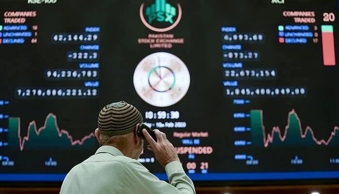 A broker talks on phone as he looks at an index board showing the latest share prices at the PSX in Karachi on February 10, 2023. — AFP