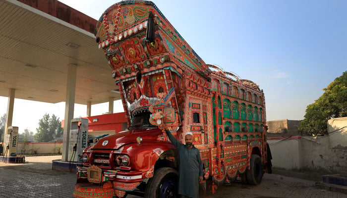 A truck driver, poses next to his decorated vehicle at a fuel station on the outskirts of Peshawar on November 21, 2023. — Reuters