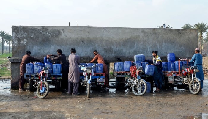 Vendors load cans of drinking water for sale on their motorcycle carts, as they fill them from a private water supply plant in Jacobabad on February 18, 2025. — AFP